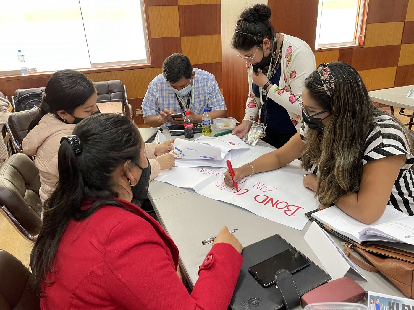 Union leaders in masks gather around a table, one writing a slogan in red marker on a large sheet of paper