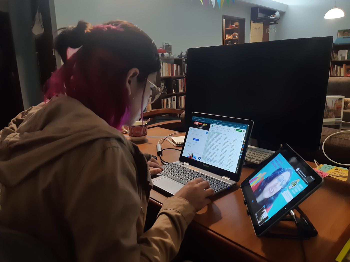 Melanie at a laptop and tablet at home, managing an online meeting