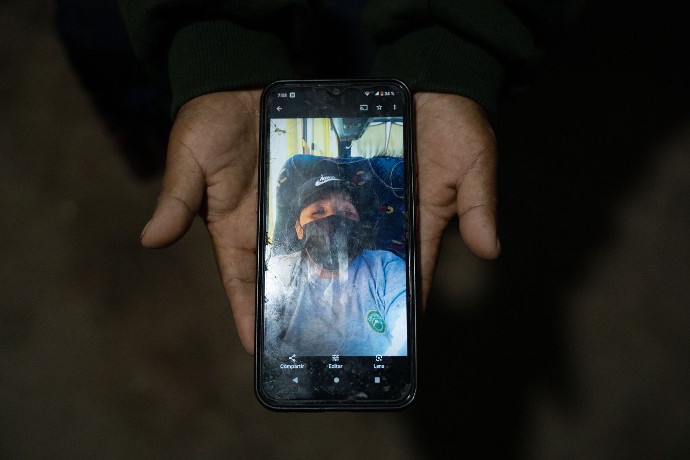 Hands holding a cracked phone that shows a selfie of a worker in a mask