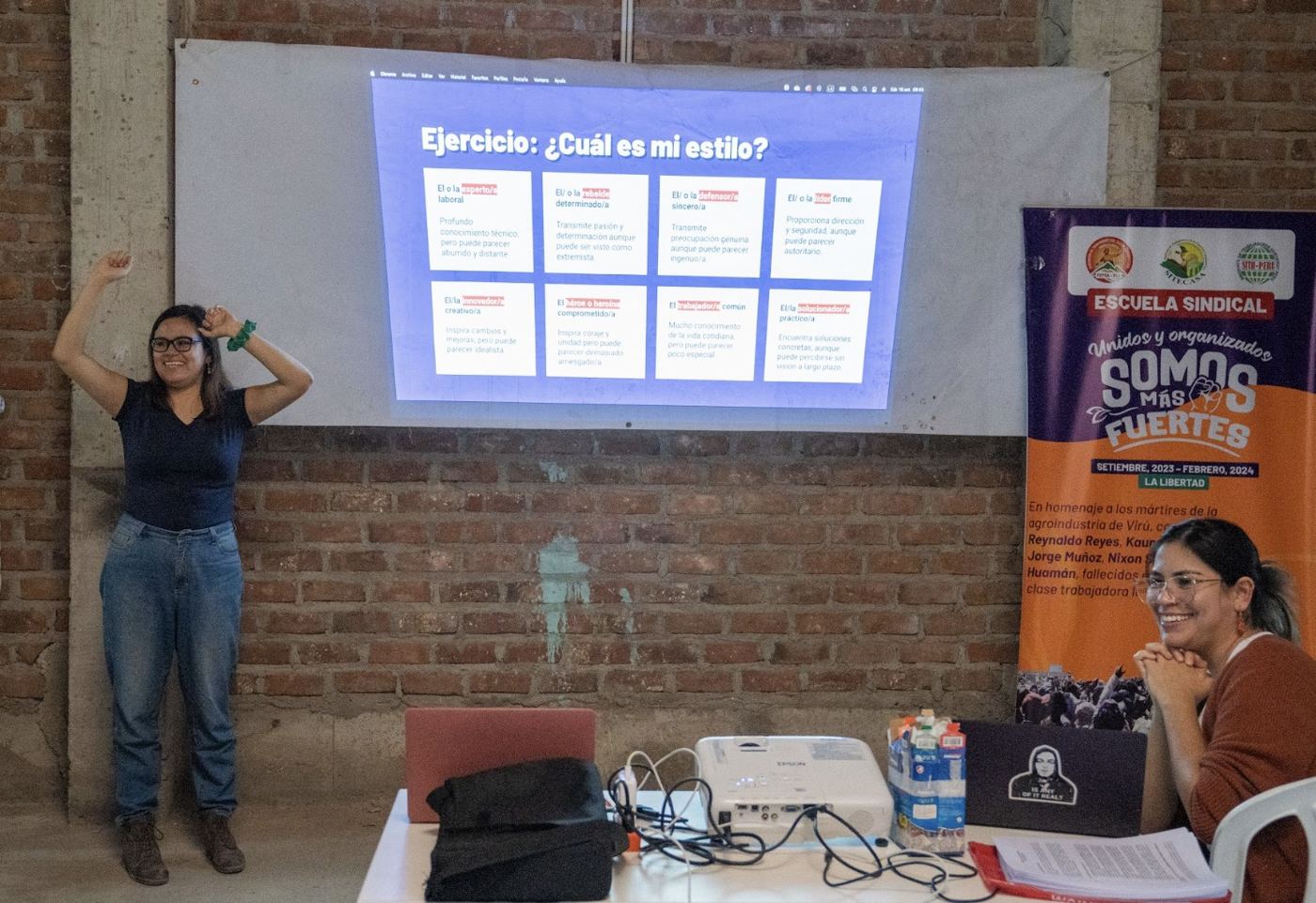 A facilitator raises her arms beside a projected exercise slide at a union school