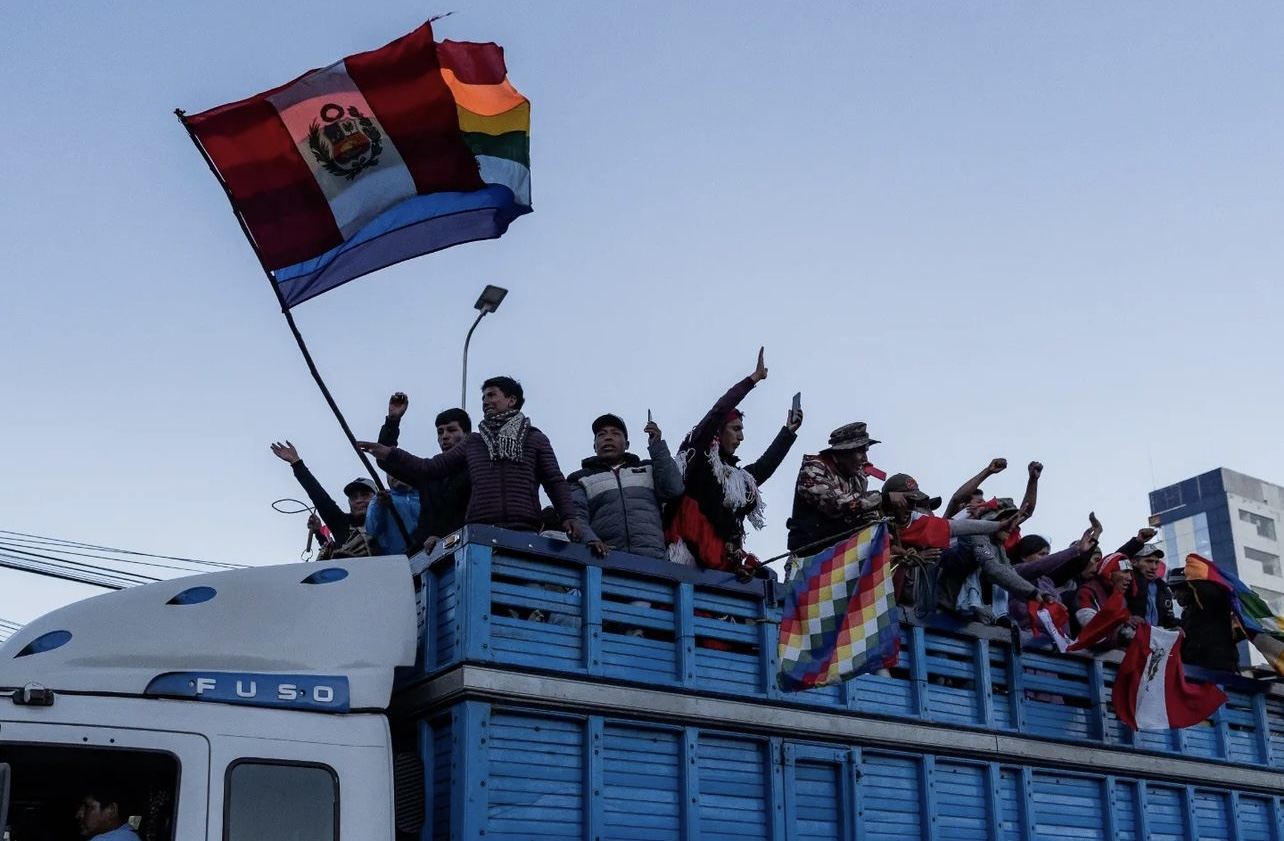 Protesters ride on top of a blue truck toward Lima, waving Peruvian and wiphala flags. Photo: Luis Javier Maguiña