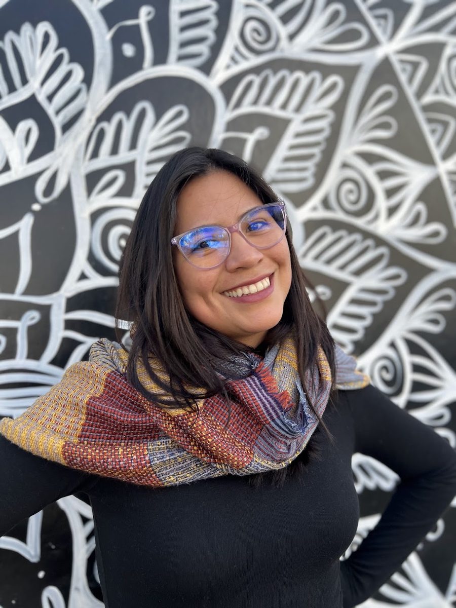 Melanie Lopez del Pozo smiling in front of a black and white mural, wearing a woven scarf
