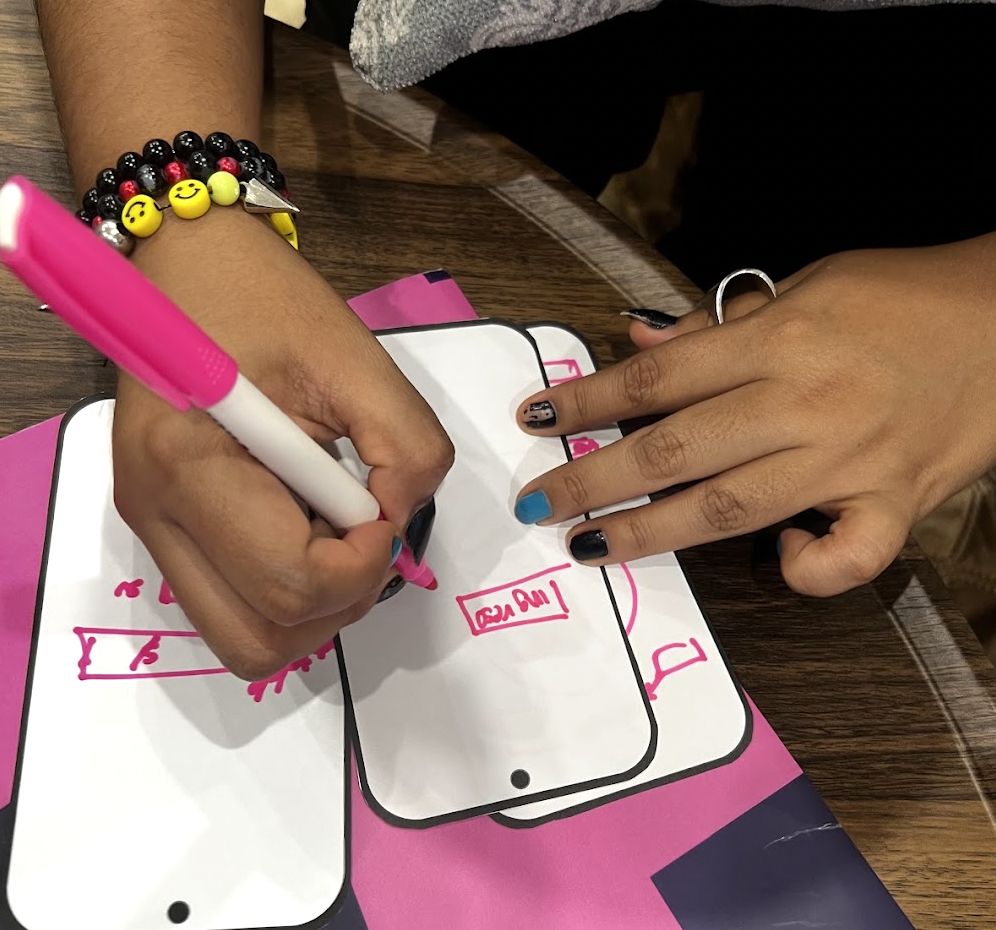 Hands sketching app screens in pink marker on paper phone templates
